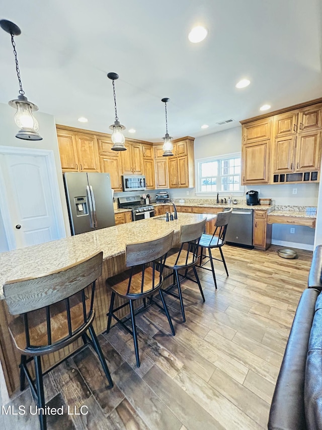 kitchen with decorative light fixtures, stainless steel appliances, a breakfast bar, and an island with sink