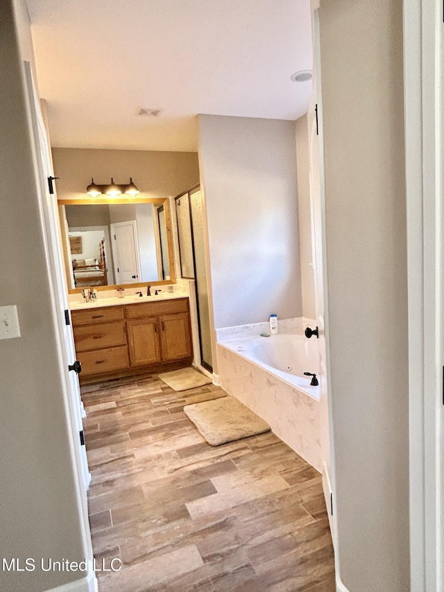 bathroom with vanity, wood-type flooring, and tiled tub