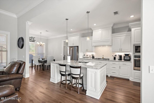 kitchen featuring white cabinetry, hanging light fixtures, a kitchen island with sink, stainless steel appliances, and light stone countertops