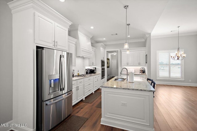 kitchen with sink, hanging light fixtures, stainless steel appliances, a kitchen island with sink, and white cabinets