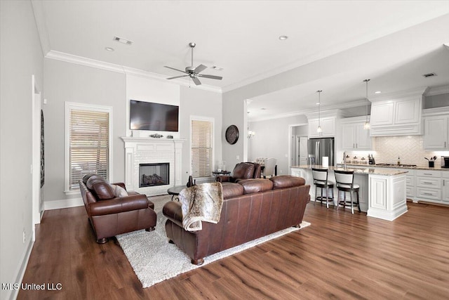 living room featuring dark wood-type flooring, ceiling fan, ornamental molding, and sink