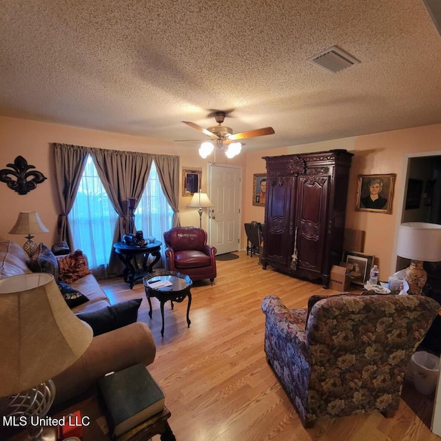 living room featuring ceiling fan, a textured ceiling, and light wood-type flooring