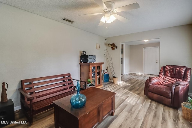 living room with ceiling fan, a textured ceiling, and light hardwood / wood-style flooring