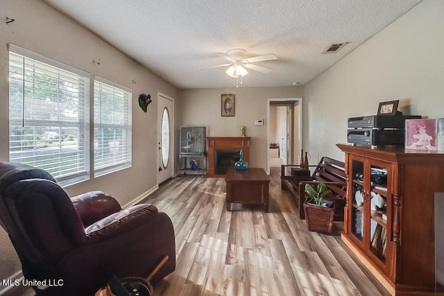 living room with ceiling fan, a textured ceiling, and light hardwood / wood-style flooring