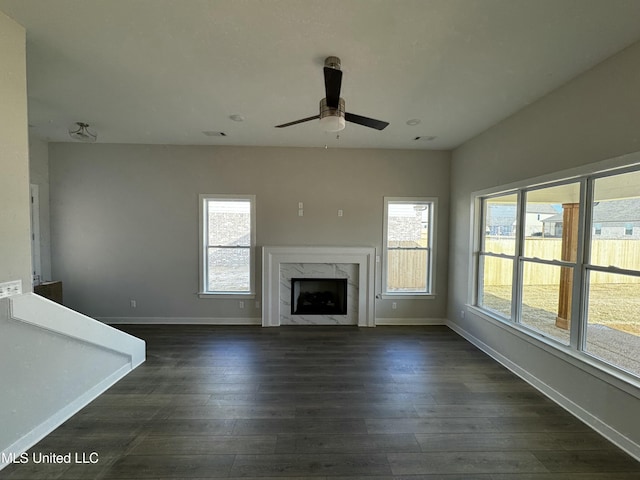 unfurnished living room with dark wood-type flooring, ceiling fan, a high end fireplace, and plenty of natural light