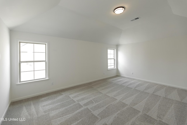 empty room with light colored carpet, vaulted ceiling, visible vents, and baseboards