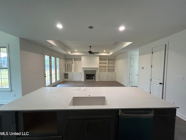 kitchen with a raised ceiling, ceiling fan, a center island with sink, and plenty of natural light