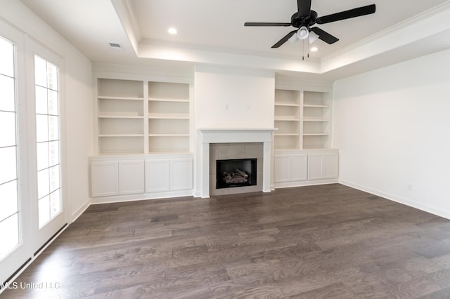 unfurnished living room featuring a tray ceiling, dark wood-style flooring, built in features, a ceiling fan, and ornamental molding