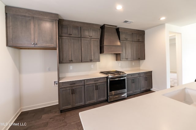 kitchen featuring a sink, visible vents, dark wood-type flooring, stainless steel gas range oven, and premium range hood