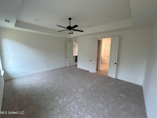 unfurnished bedroom featuring carpet flooring, a tray ceiling, and ceiling fan