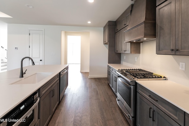 kitchen with a sink, dark wood finished floors, custom range hood, light countertops, and appliances with stainless steel finishes