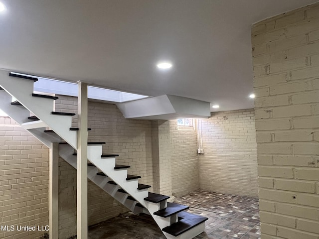 finished basement featuring brick floor, recessed lighting, brick wall, and stairs