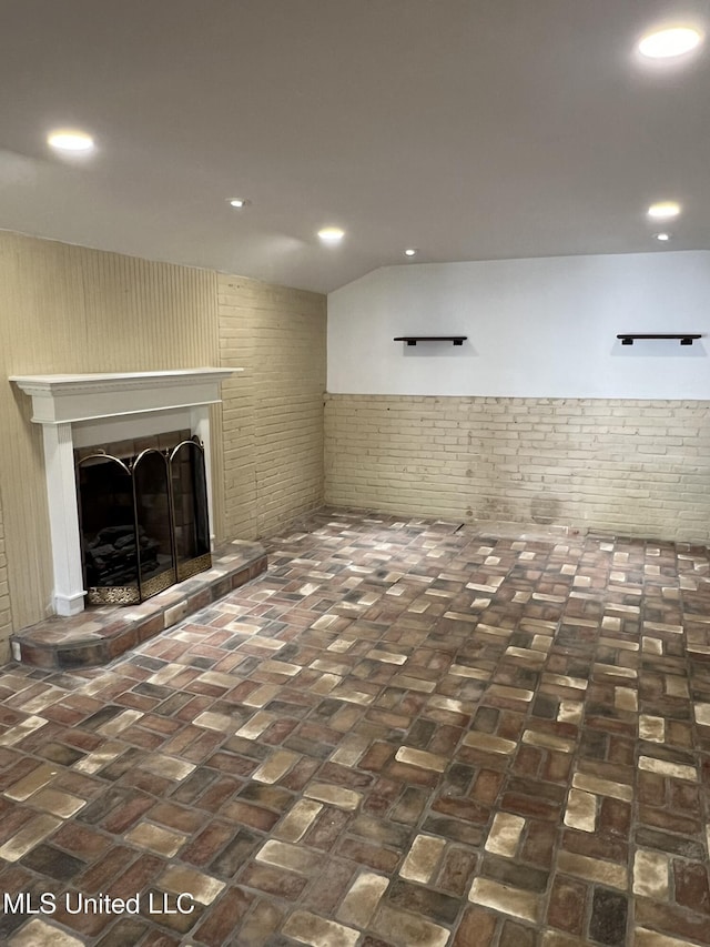 below grade area featuring a wainscoted wall, brick floor, a fireplace with raised hearth, and recessed lighting