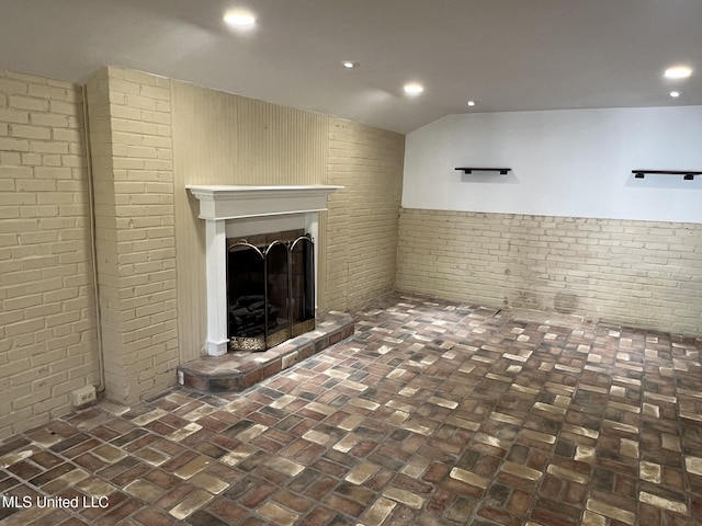 unfurnished living room with brick floor, recessed lighting, a fireplace with raised hearth, wainscoting, and brick wall