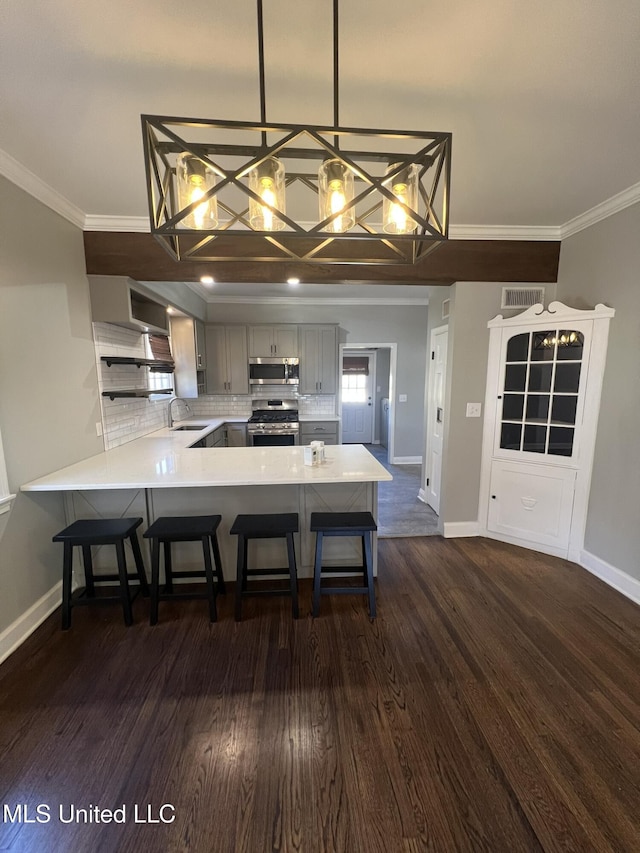 kitchen with a peninsula, stainless steel appliances, light countertops, pendant lighting, and a sink