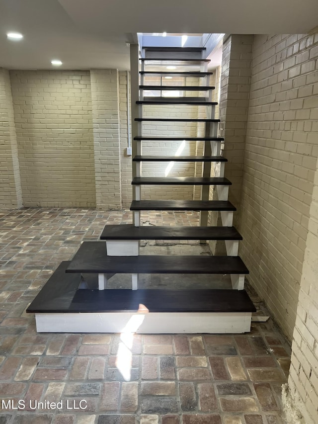 stairway featuring brick floor, recessed lighting, and brick wall