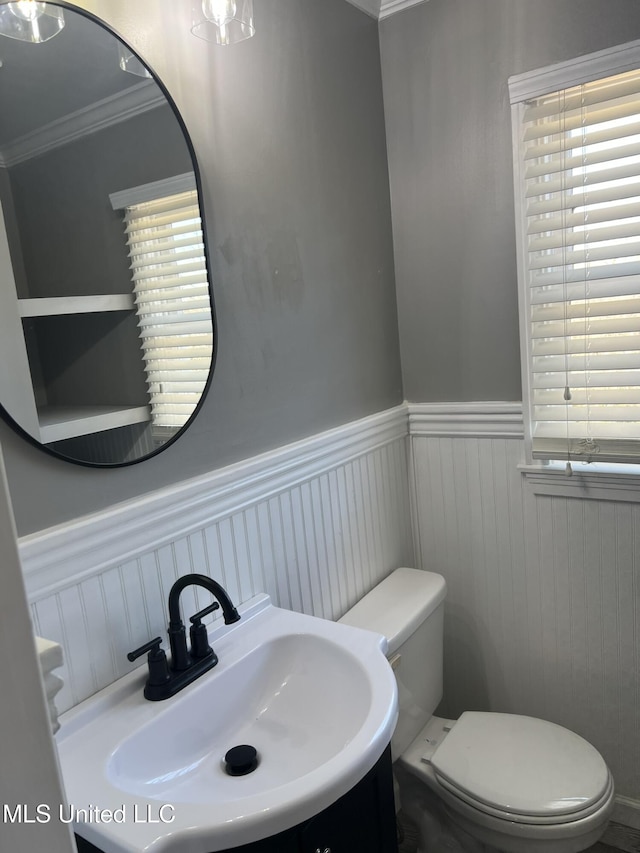 bathroom featuring wainscoting, a sink, toilet, and crown molding