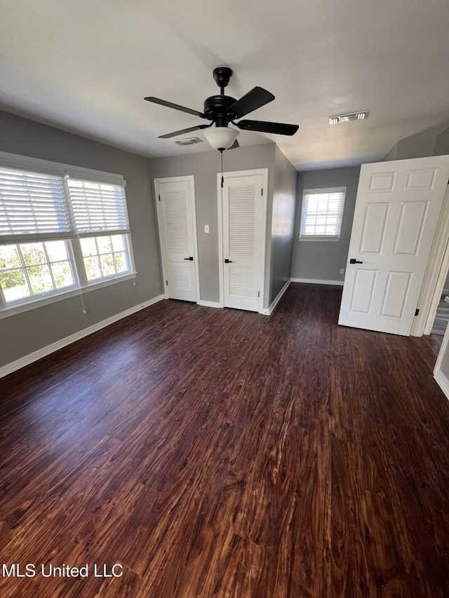 unfurnished bedroom featuring dark wood-type flooring, a ceiling fan, visible vents, and baseboards