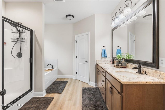 bathroom with a stall shower, wood finished floors, a garden tub, double vanity, and baseboards