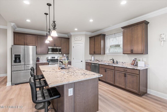 kitchen with stainless steel appliances, a sink, a breakfast bar, light wood-type flooring, and baseboards