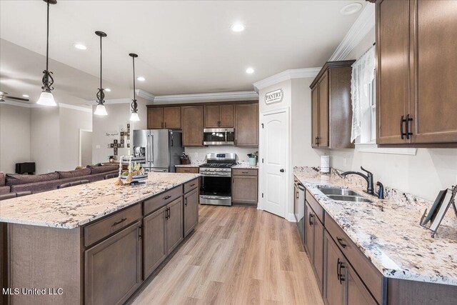 kitchen with stainless steel appliances, a sink, ornamental molding, open floor plan, and light wood-style flooring