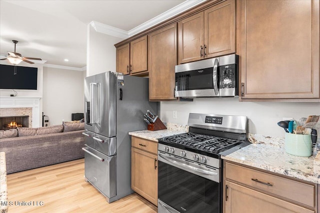 kitchen with appliances with stainless steel finishes, a ceiling fan, ornamental molding, open floor plan, and light wood-style flooring