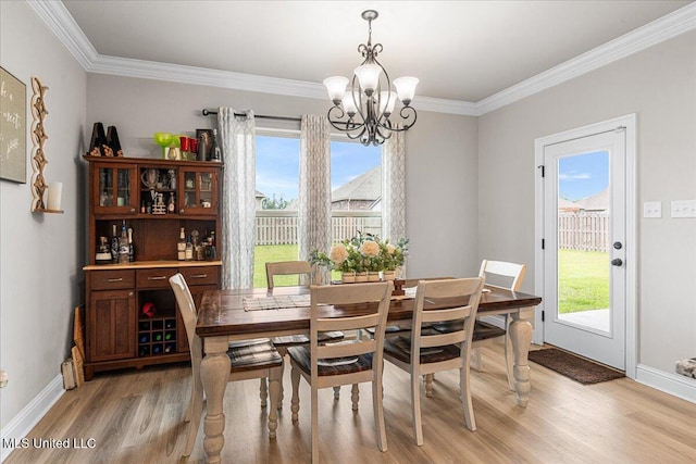 dining area with a chandelier, light wood finished floors, crown molding, healthy amount of natural light, and baseboards