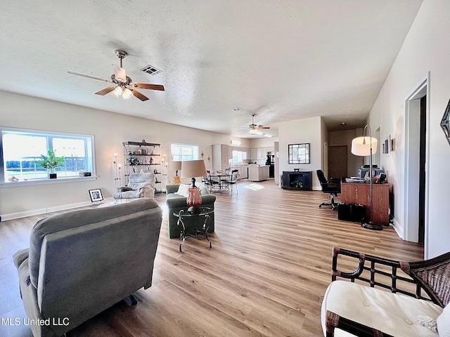 living room with a textured ceiling, ceiling fan, visible vents, baseboards, and light wood finished floors