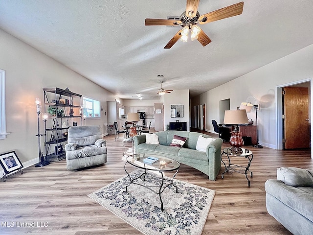 living area featuring light wood-type flooring, baseboards, vaulted ceiling, and a textured ceiling