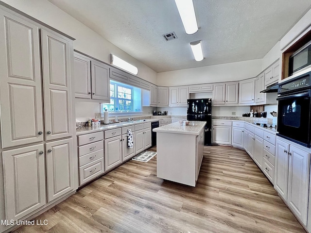 kitchen featuring black appliances, a kitchen island, visible vents, and light wood finished floors