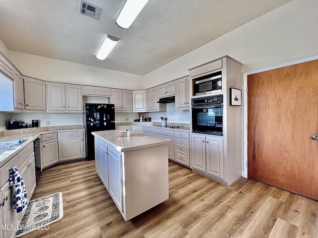 kitchen with black appliances, light wood-style flooring, a kitchen island, and under cabinet range hood