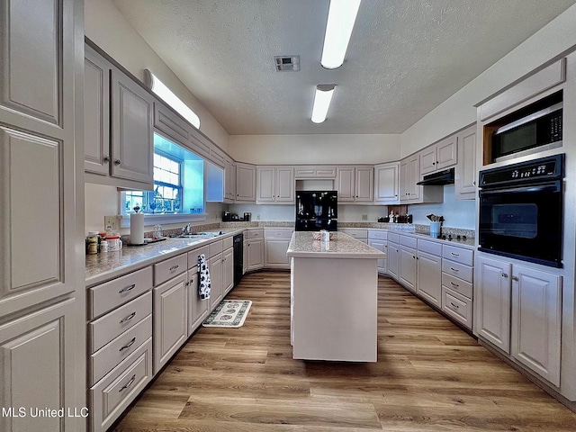 kitchen featuring visible vents, a kitchen island, under cabinet range hood, light countertops, and black appliances