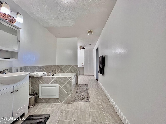 full bath featuring a textured ceiling, vanity, a bath, and tile walls