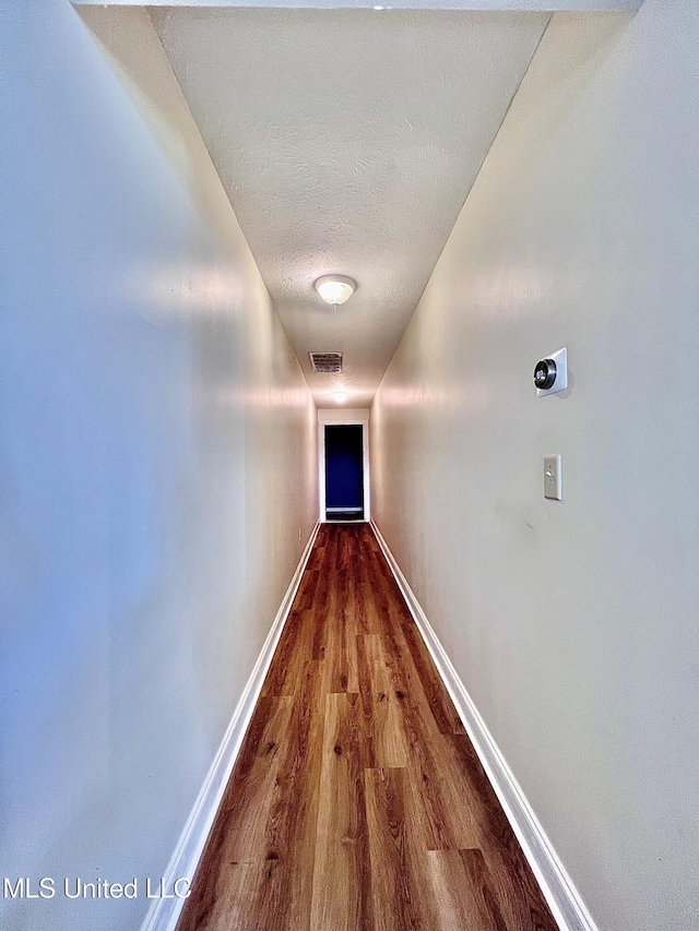 corridor featuring a textured ceiling, wood finished floors, visible vents, and baseboards