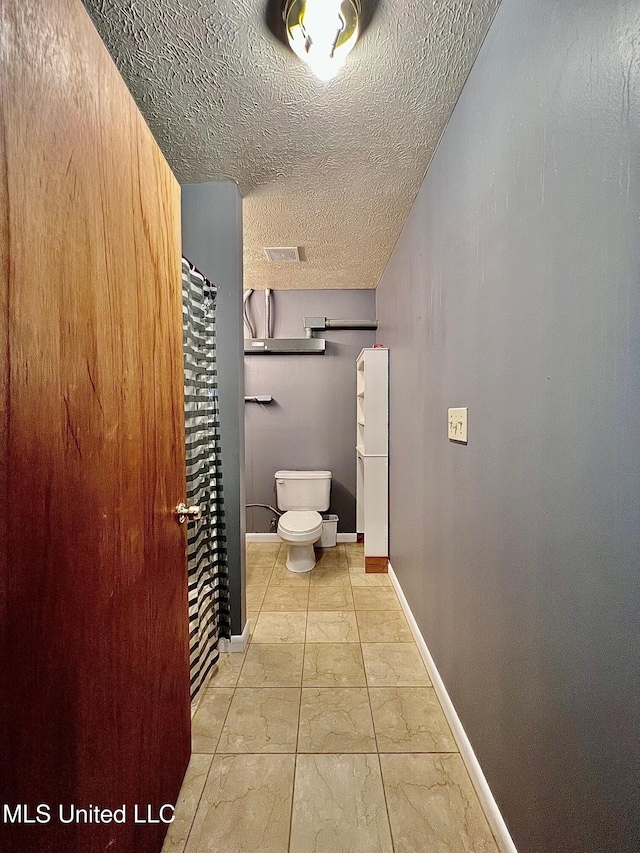 bathroom with visible vents, toilet, a textured ceiling, and baseboards