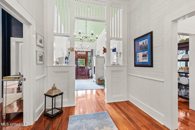 hall featuring hardwood / wood-style flooring, a towering ceiling, and an inviting chandelier