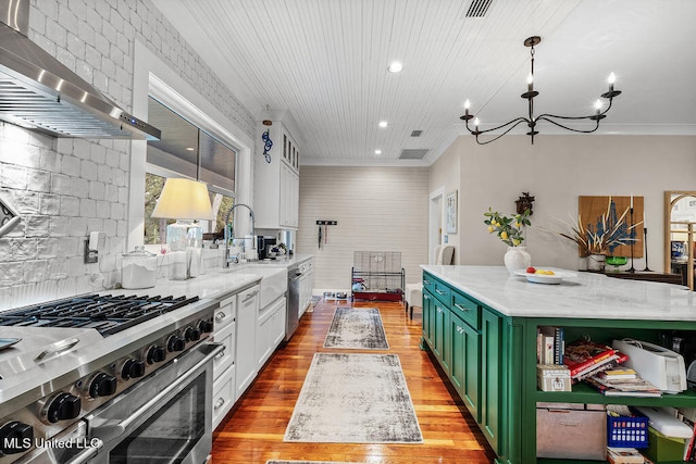 kitchen with wall chimney range hood, green cabinets, stainless steel appliances, light stone counters, and light hardwood / wood-style floors