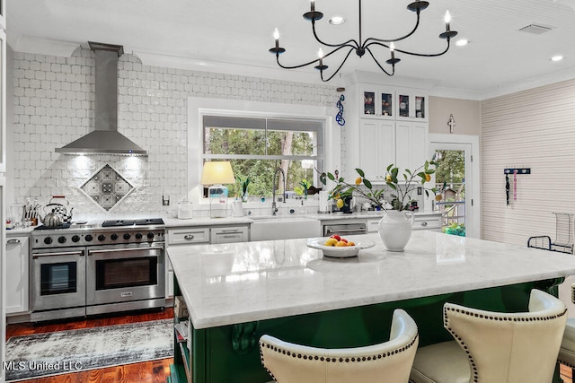 kitchen featuring wall chimney exhaust hood, range with two ovens, a center island, pendant lighting, and white cabinets