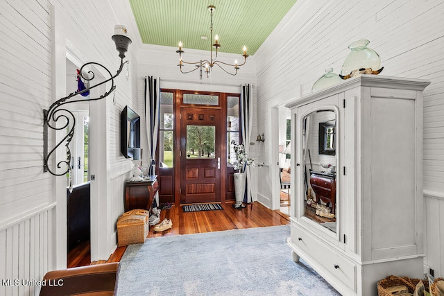 foyer entrance with ornamental molding, a chandelier, hardwood / wood-style flooring, and wood walls