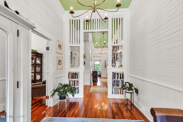 foyer entrance with wood walls, a chandelier, and dark wood-type flooring