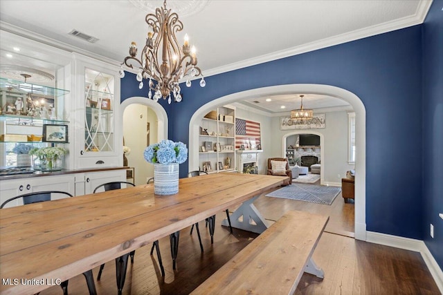 dining space with visible vents, a chandelier, ornamental molding, a fireplace, and wood finished floors