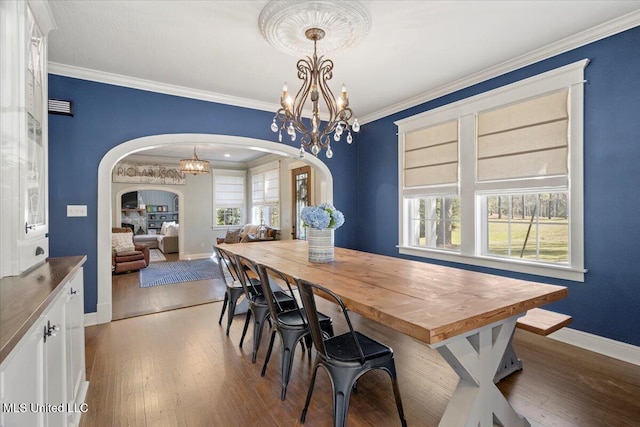 dining space with arched walkways, crown molding, an inviting chandelier, and hardwood / wood-style floors