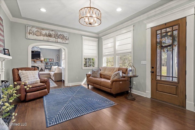 living area featuring wood finished floors, baseboards, a fireplace, arched walkways, and crown molding