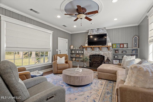 living room with visible vents, a stone fireplace, crown molding, and wood finished floors