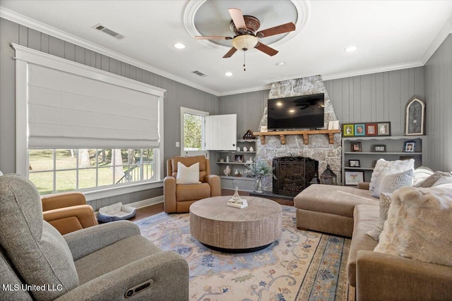 living room featuring visible vents, wood finished floors, a stone fireplace, and ornamental molding