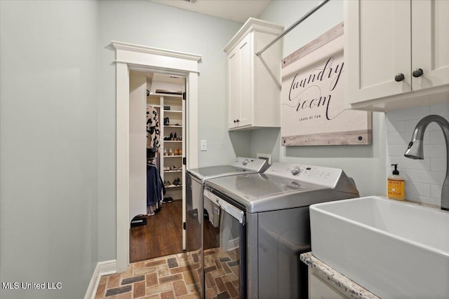 laundry area featuring baseboards, cabinet space, brick floor, a sink, and washer and clothes dryer