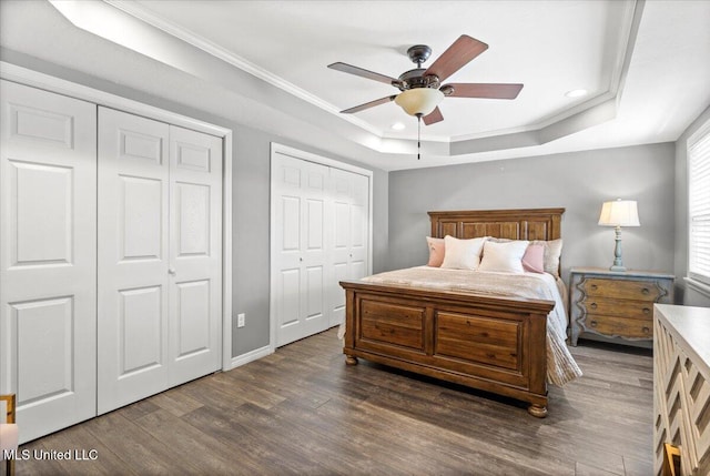 bedroom featuring dark wood finished floors, two closets, a raised ceiling, and ornamental molding