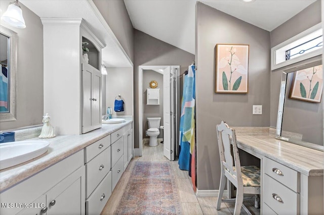 bathroom with double vanity, toilet, vaulted ceiling, and a sink