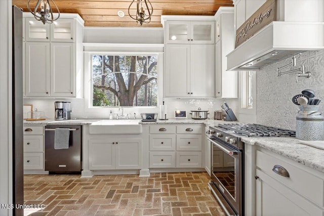 kitchen featuring stainless steel appliances, brick floor, white cabinetry, wall chimney exhaust hood, and a sink