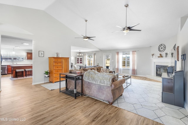 living room with vaulted ceiling, ceiling fan with notable chandelier, and light hardwood / wood-style flooring